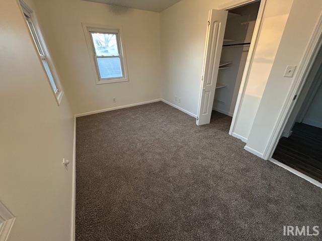 unfurnished bedroom with dark colored carpet and a closet