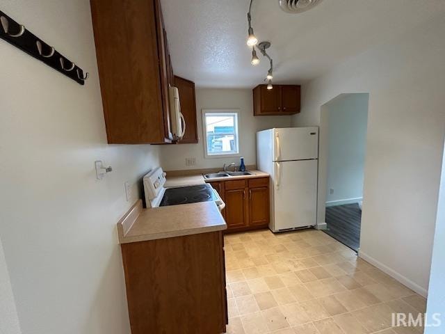 kitchen with a textured ceiling, white appliances, sink, and track lighting