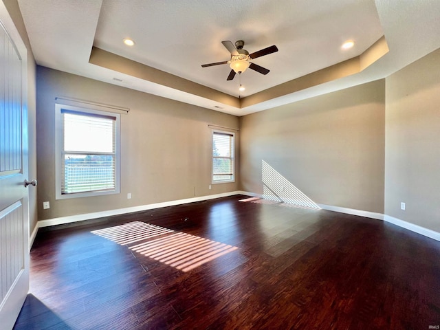 empty room featuring a tray ceiling, dark hardwood / wood-style floors, a healthy amount of sunlight, and ceiling fan