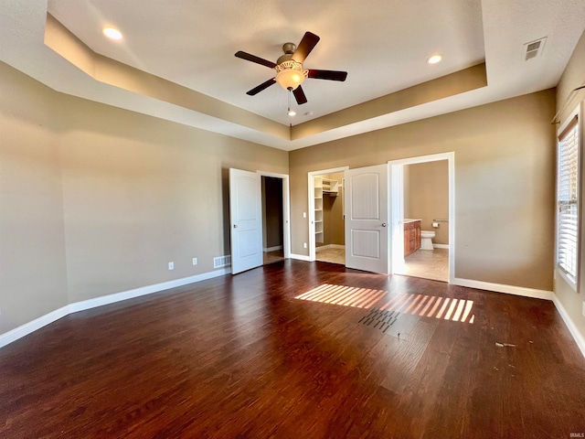 unfurnished bedroom featuring dark hardwood / wood-style floors, a closet, a spacious closet, a raised ceiling, and ceiling fan