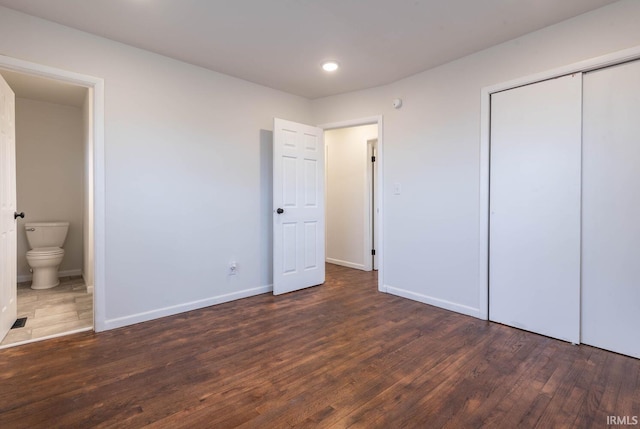 unfurnished bedroom featuring ensuite bathroom, dark hardwood / wood-style floors, and a closet