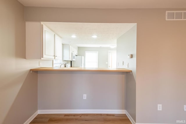 kitchen with white fridge, light hardwood / wood-style floors, white cabinetry, and kitchen peninsula