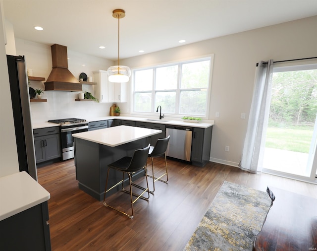 kitchen featuring custom exhaust hood, hanging light fixtures, appliances with stainless steel finishes, a kitchen bar, and a center island