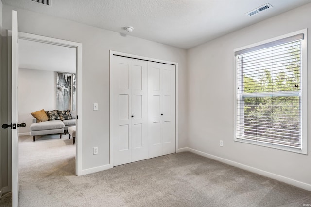 unfurnished bedroom with a closet, a textured ceiling, multiple windows, and light colored carpet