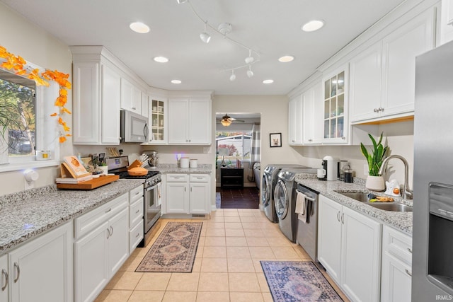 kitchen with sink, white cabinets, light tile patterned floors, appliances with stainless steel finishes, and washing machine and clothes dryer