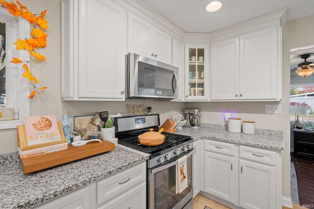 kitchen with light stone countertops, light hardwood / wood-style floors, appliances with stainless steel finishes, and white cabinets