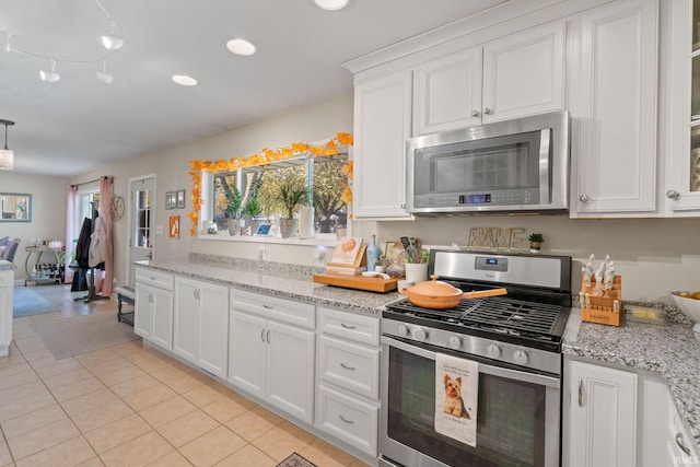 kitchen with appliances with stainless steel finishes, white cabinets, light stone counters, and light tile patterned floors