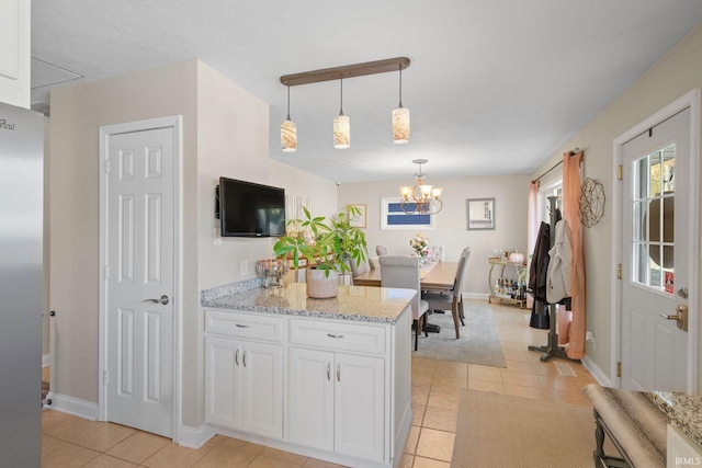 kitchen featuring light tile patterned floors, white cabinetry, light stone countertops, pendant lighting, and a notable chandelier