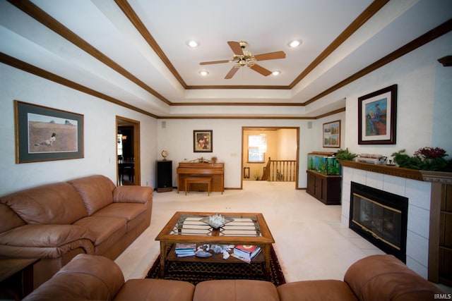 carpeted living room with crown molding, a tray ceiling, a fireplace, and ceiling fan