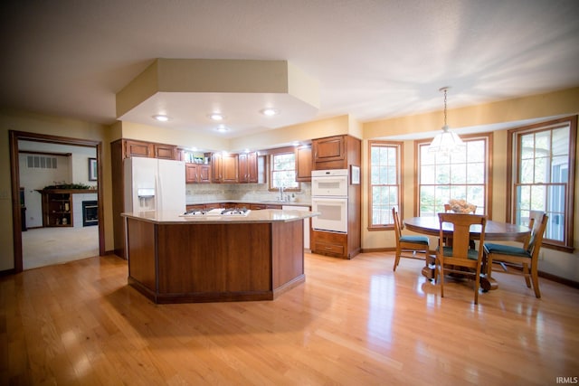 kitchen featuring tasteful backsplash, hanging light fixtures, a kitchen island, light hardwood / wood-style floors, and white appliances