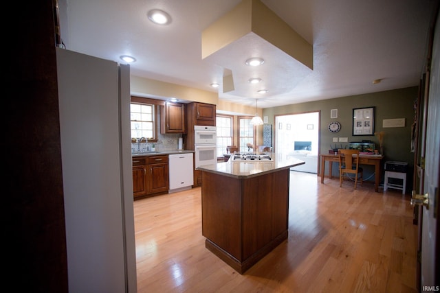 kitchen with white appliances, sink, backsplash, light hardwood / wood-style floors, and pendant lighting