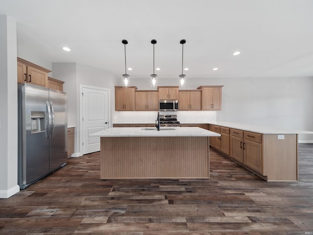 kitchen with dark wood-type flooring, appliances with stainless steel finishes, decorative light fixtures, and a kitchen island with sink