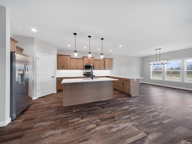 kitchen with stainless steel appliances, hanging light fixtures, a center island with sink, and dark wood-type flooring