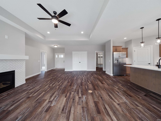 unfurnished living room featuring dark hardwood / wood-style flooring, a tray ceiling, a tile fireplace, and ceiling fan