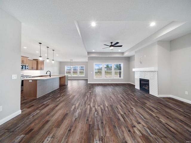 unfurnished living room with a textured ceiling, sink, dark wood-type flooring, a tile fireplace, and ceiling fan