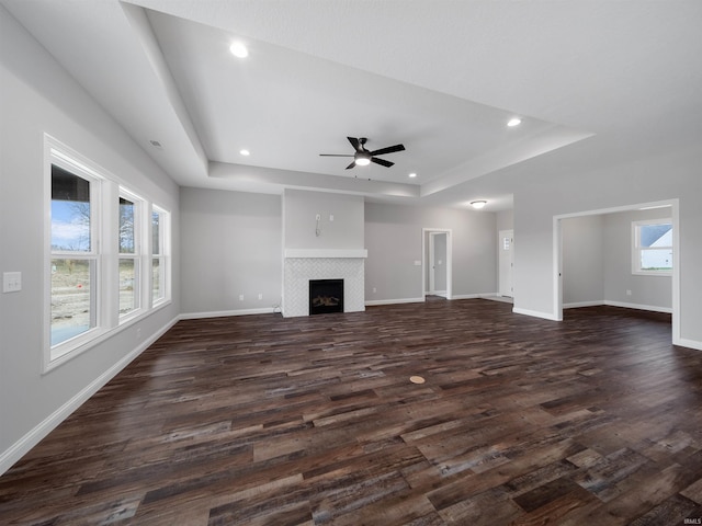 unfurnished living room with a fireplace, ceiling fan, dark hardwood / wood-style flooring, and a tray ceiling