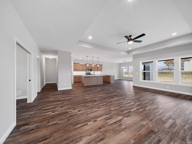 unfurnished living room featuring ceiling fan with notable chandelier, sink, and dark hardwood / wood-style flooring