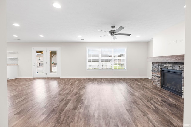 unfurnished living room with a stone fireplace, ceiling fan, and dark hardwood / wood-style floors