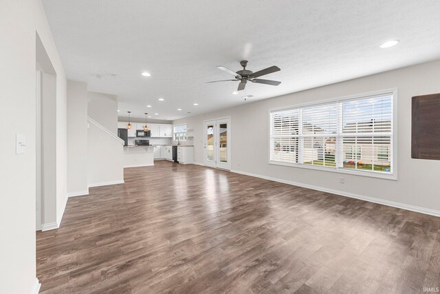 unfurnished living room with ceiling fan, a textured ceiling, and dark hardwood / wood-style flooring