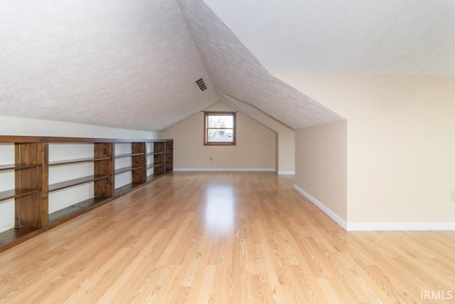 bonus room with light hardwood / wood-style floors, a textured ceiling, and lofted ceiling