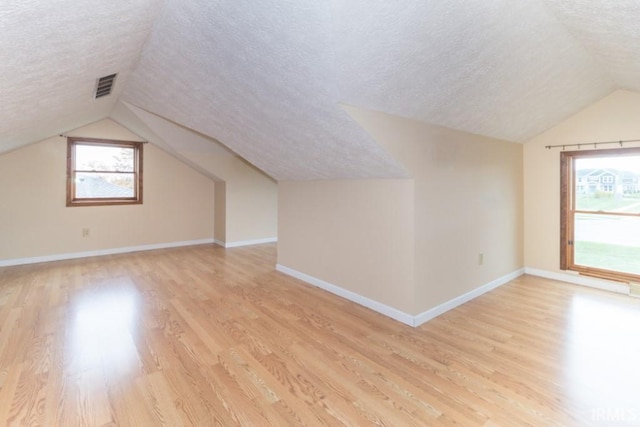 additional living space featuring light wood-type flooring, lofted ceiling, and a textured ceiling