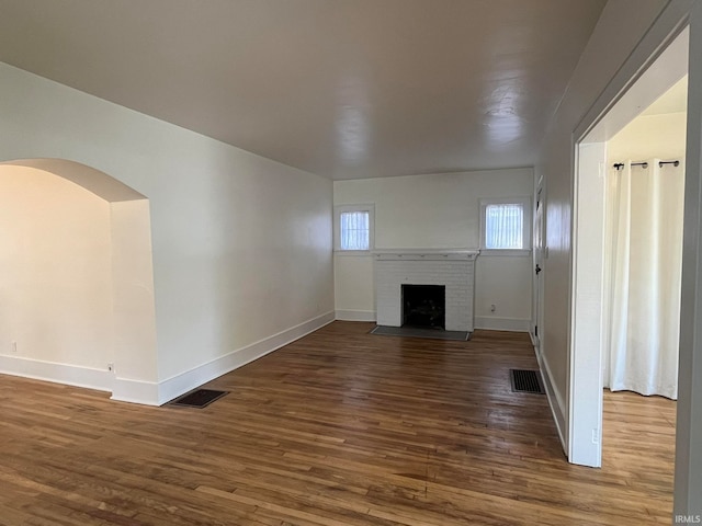 unfurnished living room with a brick fireplace and dark hardwood / wood-style floors