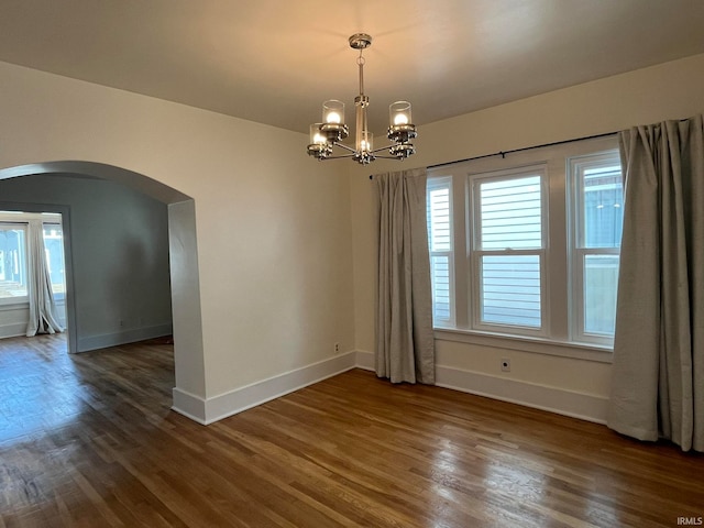 spare room featuring dark wood-type flooring and a notable chandelier