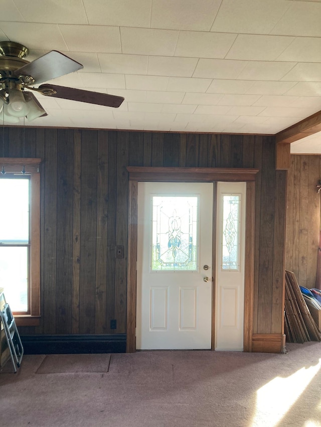 entrance foyer with carpet flooring, ceiling fan, and wood walls