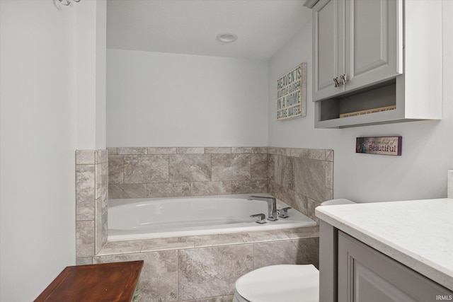 bathroom featuring vanity, tiled tub, and toilet