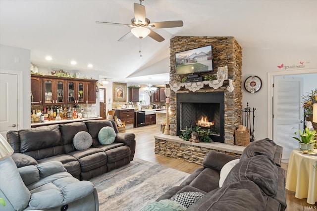 living room with light hardwood / wood-style flooring, vaulted ceiling, ceiling fan with notable chandelier, and a fireplace