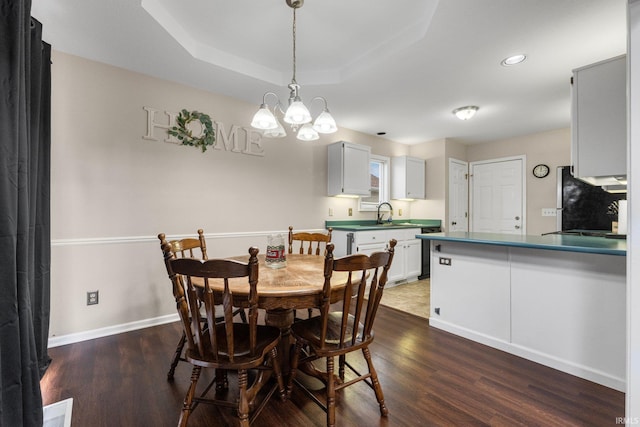 dining room featuring dark hardwood / wood-style floors, a notable chandelier, sink, and a tray ceiling