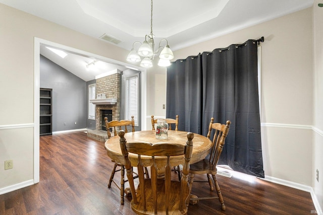 dining area with an inviting chandelier, a raised ceiling, dark hardwood / wood-style floors, and a brick fireplace