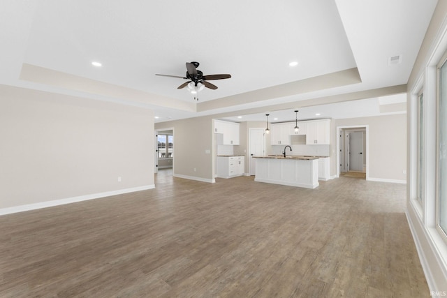 unfurnished living room featuring light hardwood / wood-style flooring, a raised ceiling, ceiling fan, and sink