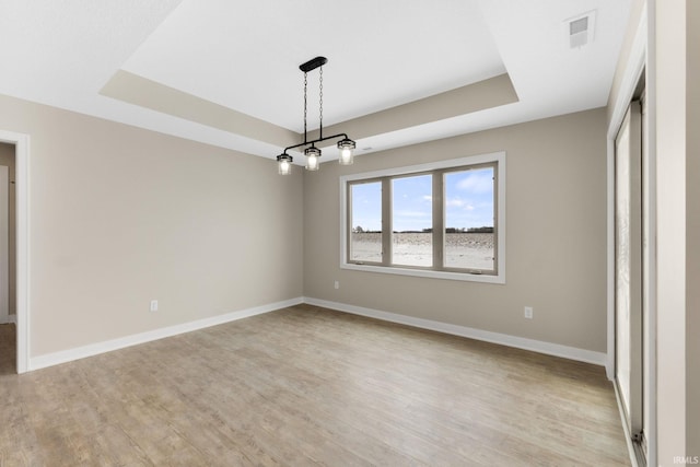 empty room featuring a tray ceiling and light hardwood / wood-style flooring