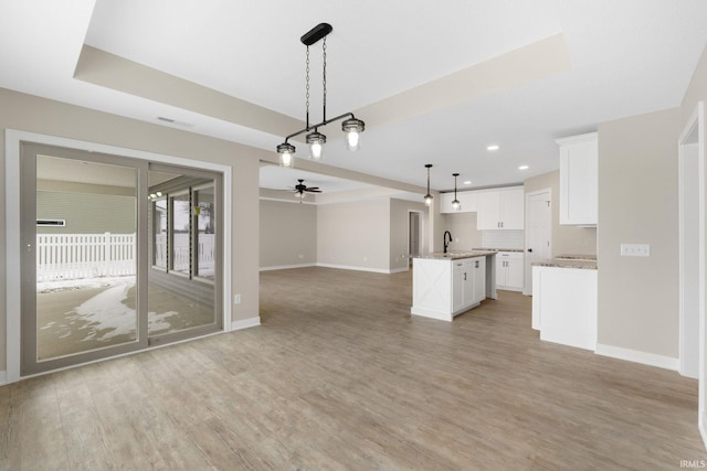 unfurnished living room with light wood-type flooring, a raised ceiling, and sink