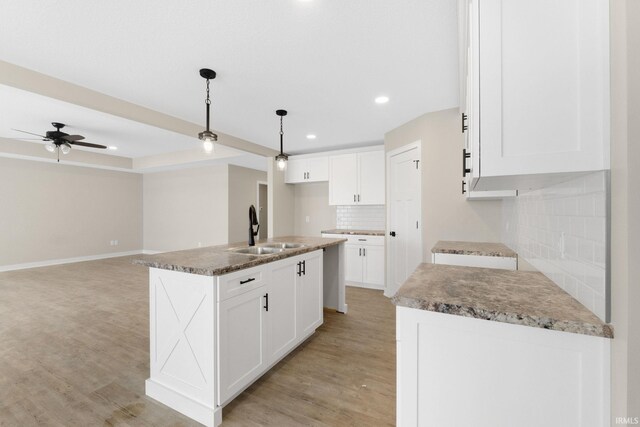 kitchen featuring pendant lighting, backsplash, white cabinets, sink, and an island with sink