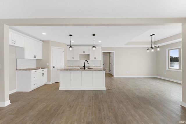 kitchen with white cabinets, decorative backsplash, hanging light fixtures, and an island with sink