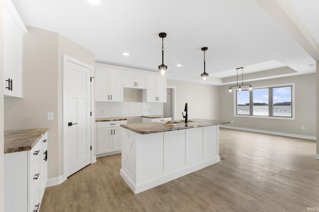 kitchen with pendant lighting, sink, white cabinetry, and an island with sink