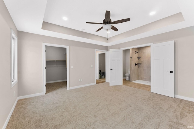 unfurnished bedroom with a raised ceiling, ensuite bath, ceiling fan, and a walk in closet