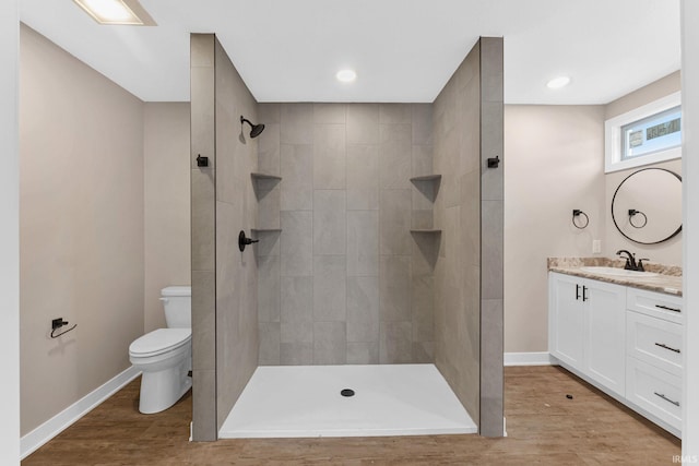 bathroom with hardwood / wood-style floors, vanity, toilet, and a tile shower