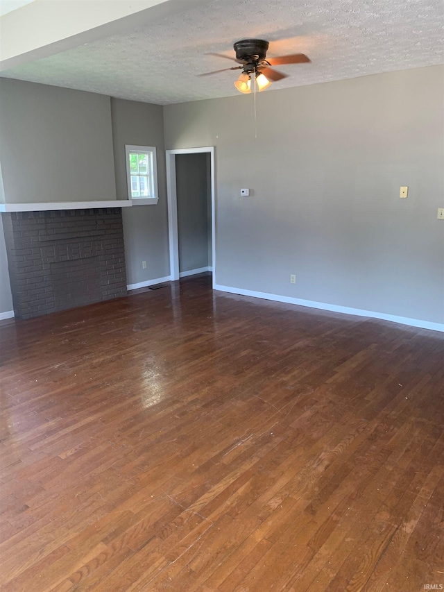 unfurnished living room with a textured ceiling, a fireplace, dark hardwood / wood-style floors, and ceiling fan