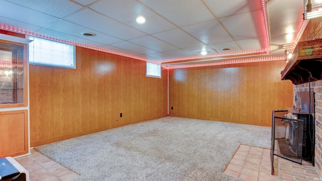 basement featuring a paneled ceiling, wooden walls, and light colored carpet