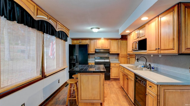 kitchen with light hardwood / wood-style flooring, a breakfast bar area, black appliances, and a center island