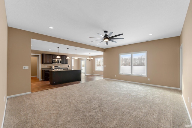 unfurnished living room featuring light colored carpet, a ceiling fan, baseboards, recessed lighting, and a chandelier