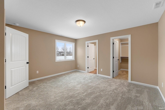 unfurnished bedroom featuring a walk in closet, light colored carpet, a textured ceiling, and a closet