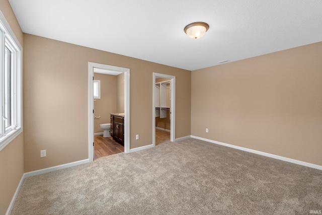 unfurnished bedroom with ensuite bathroom, a walk in closet, light colored carpet, and a closet