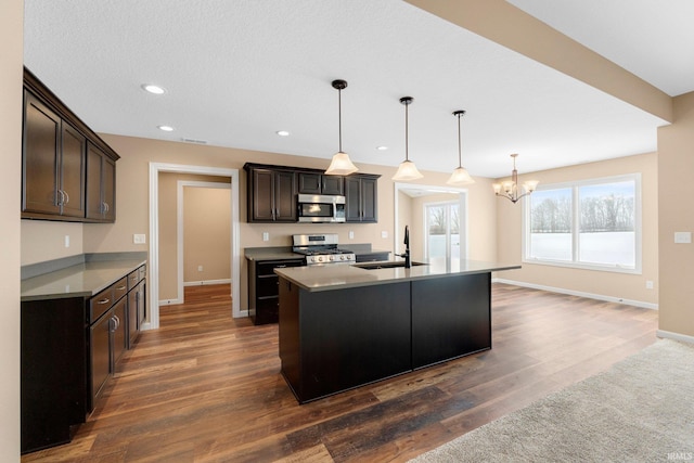 kitchen with appliances with stainless steel finishes, a sink, a chandelier, dark wood-style flooring, and baseboards