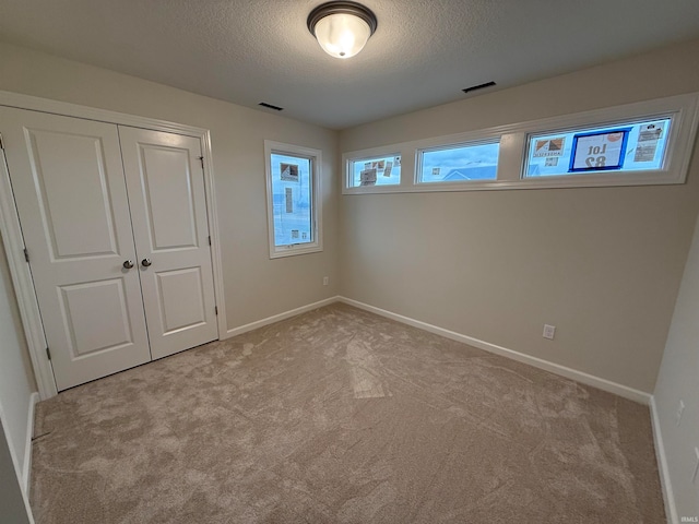 unfurnished bedroom featuring light colored carpet, a textured ceiling, and a closet