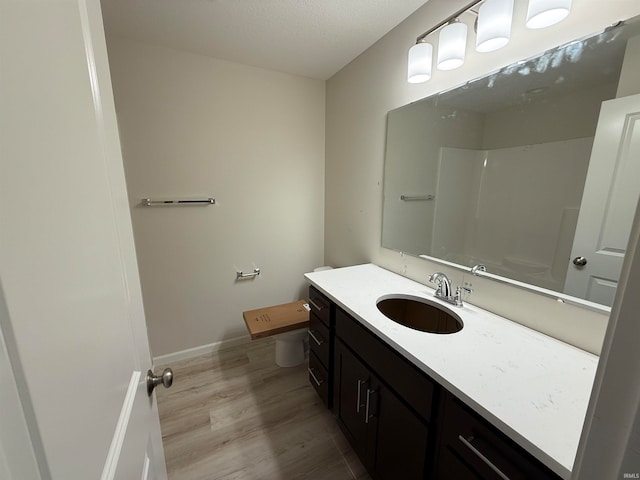 bathroom featuring wood-type flooring, walk in shower, vanity, and toilet