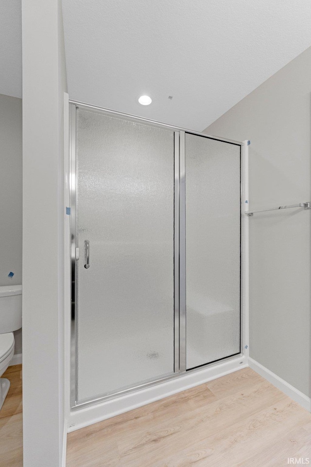 bathroom with hardwood / wood-style floors, toilet, and a shower with door